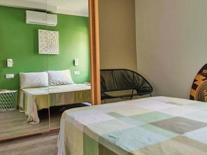 A room with a bed, a chair, a mirror, and a wall-mounted air conditioner.