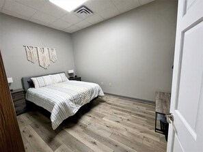 A bedroom with a bed, nightstands, a wall-mounted macrame decoration, and a wooden floor.