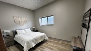 A bedroom with a bed, nightstands, a wall-mounted macrame piece, a window, and a wooden bench. - Adorable 7 bedroom place (Mitchell)