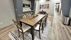 A modern dining area with a wooden table and chairs, a rug, and a kitchen in the background. - Adorable 7 bedroom place (Mitchell)