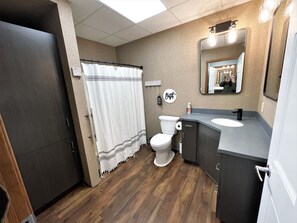 A bathroom with a wooden floor, a white toilet, a vanity with a mirror, and a shower curtain.