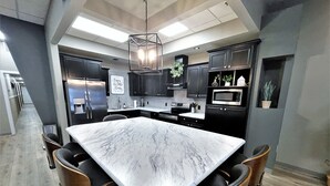 A modern kitchen with a large marble island, dark cabinetry, and stainless steel appliances. - Adorable 7 bedroom place (Mitchell)
