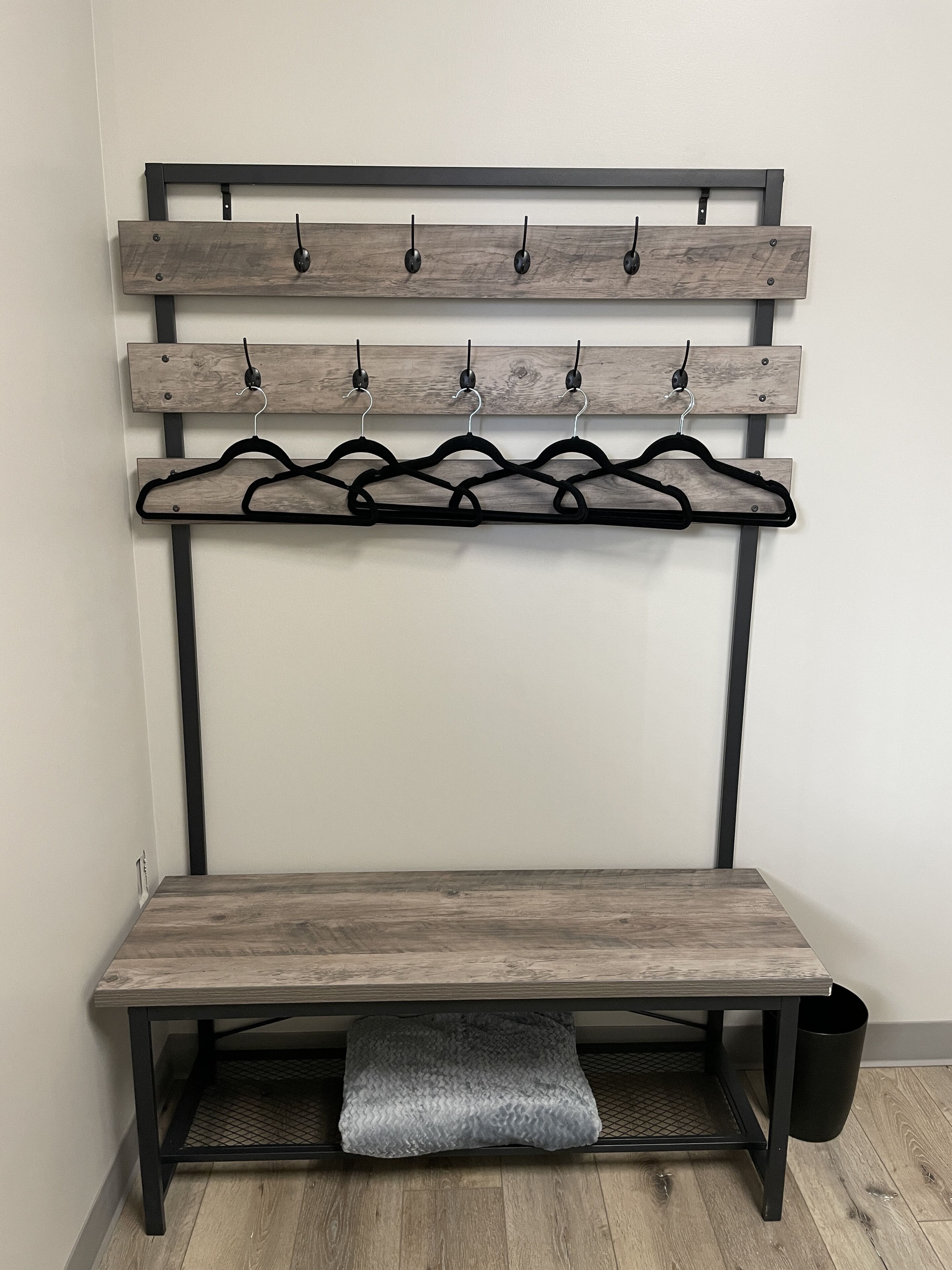 A bench with a wooden seat and backrest, a metal frame, and a coat rack with hooks and hangers.