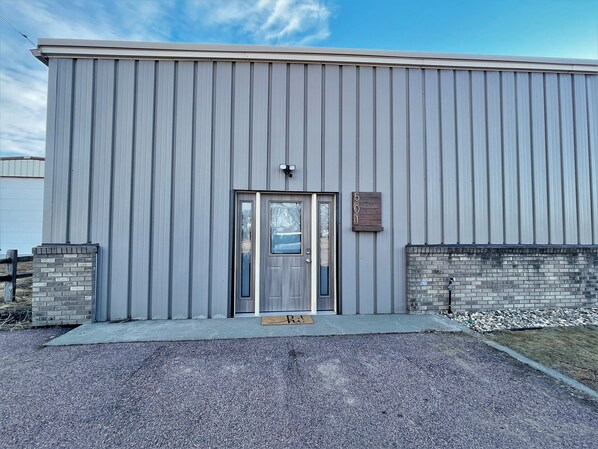 A building with a grey exterior, a metal door, and a small sign with the number 501.