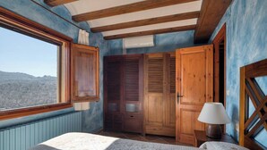 Een slaapkamer met een groot bed, een houten kledingkast en een raam met uitzicht op het landschap.