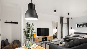 A modern living room with a sofa, a dining table set for two, a television, and a large mirror. - Bison Meadow Lodge #4 (Gardiner)