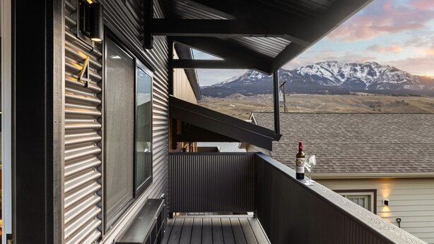 A balcony with a view of snow-capped mountains, a bottle of wine, and a glass on the railing. - Bison Meadow Lodge #4 (Gardiner)