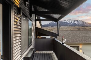 A balcony with a view of snow-capped mountains, a bottle of wine, and a glass on the railing.