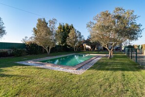 Une piscine rectangulaire bordée de pierres, entourée d’une pelouse bien entretenue et d’arbres.