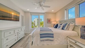 A bedroom with a bed, nightstands, a dresser, a ceiling fan, and a large window with a view of buildings and palm trees. - Beach Dream | Home w/ Ocean Views, 2 Private Pools, Rooftop Lookout and Steps to Siesta Key Beach! (Siesta Key)