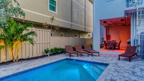 A swimming pool with lounge chairs, a covered patio area, and a view of a building with a beige exterior and a red door. - Beach Dream | Home w/ Ocean Views, 2 Private Pools, Rooftop Lookout and Steps to Siesta Key Beach! (Siesta Key)