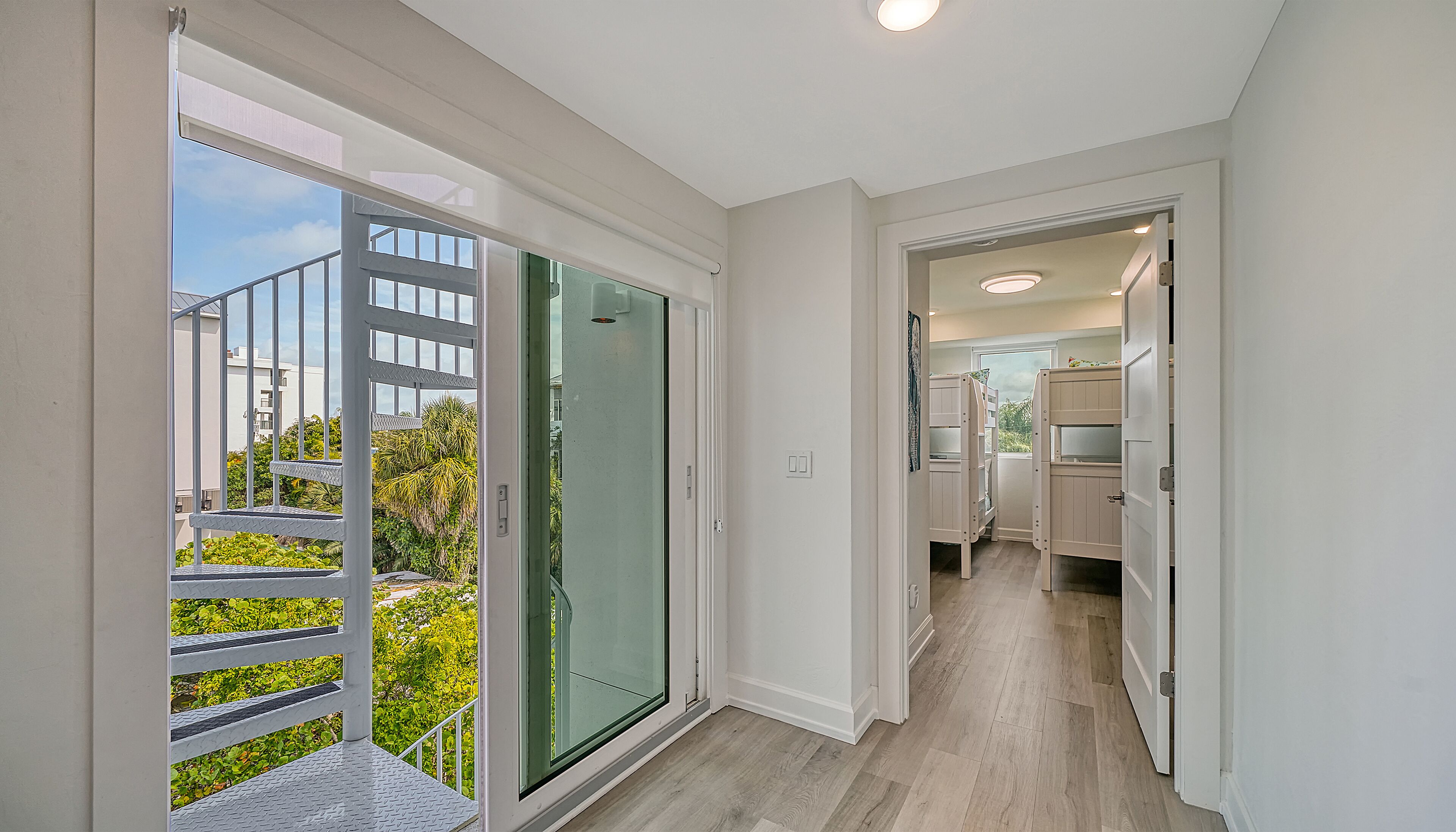 A modern apartment with a balcony, a glass door leading outside, and a kitchen area visible through an open door.