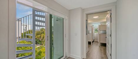 A modern apartment with a balcony, a glass door leading outside, and a kitchen area visible through an open door.