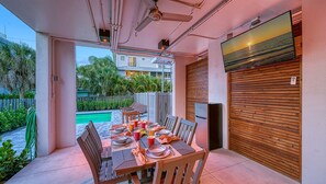 An outdoor dining area with a pool view, wooden table and chairs, and a sliding door.