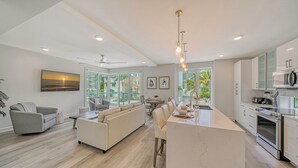 Una cocina moderna con una isla central, un comedor con sofá y vistas al exterior.