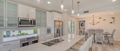A modern kitchen with a large island, stainless steel appliances, and a dining area with wicker chairs.