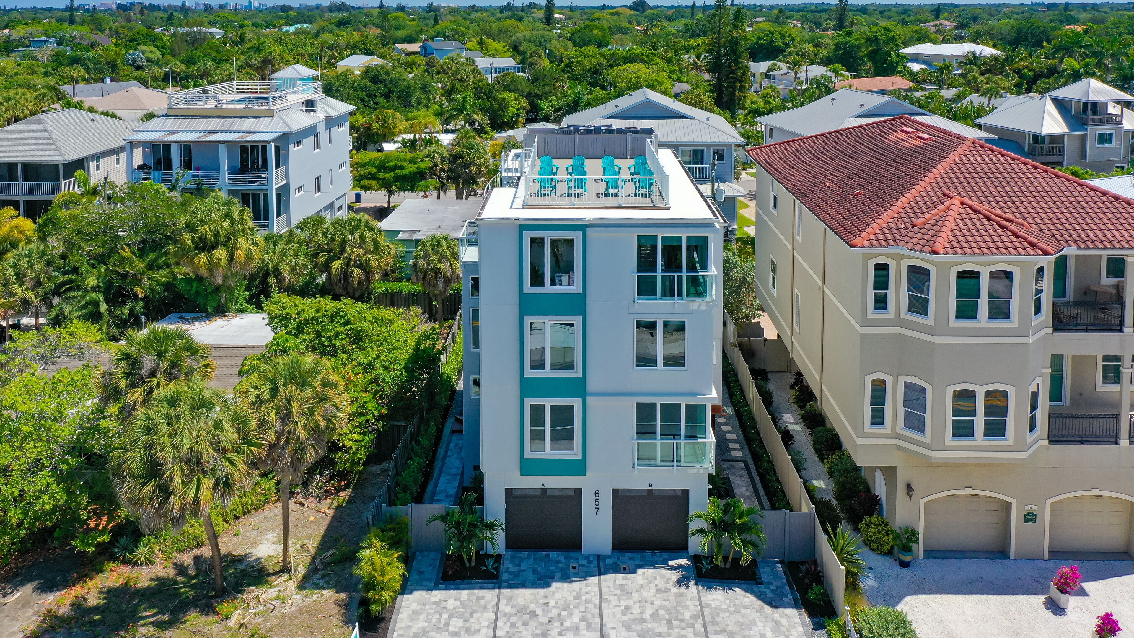 A multi-story residential building with a flat roof, a balcony with chairs, and a garage.