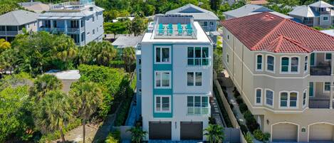 A multi-story residential building with a flat roof, a balcony with chairs, and a garage.