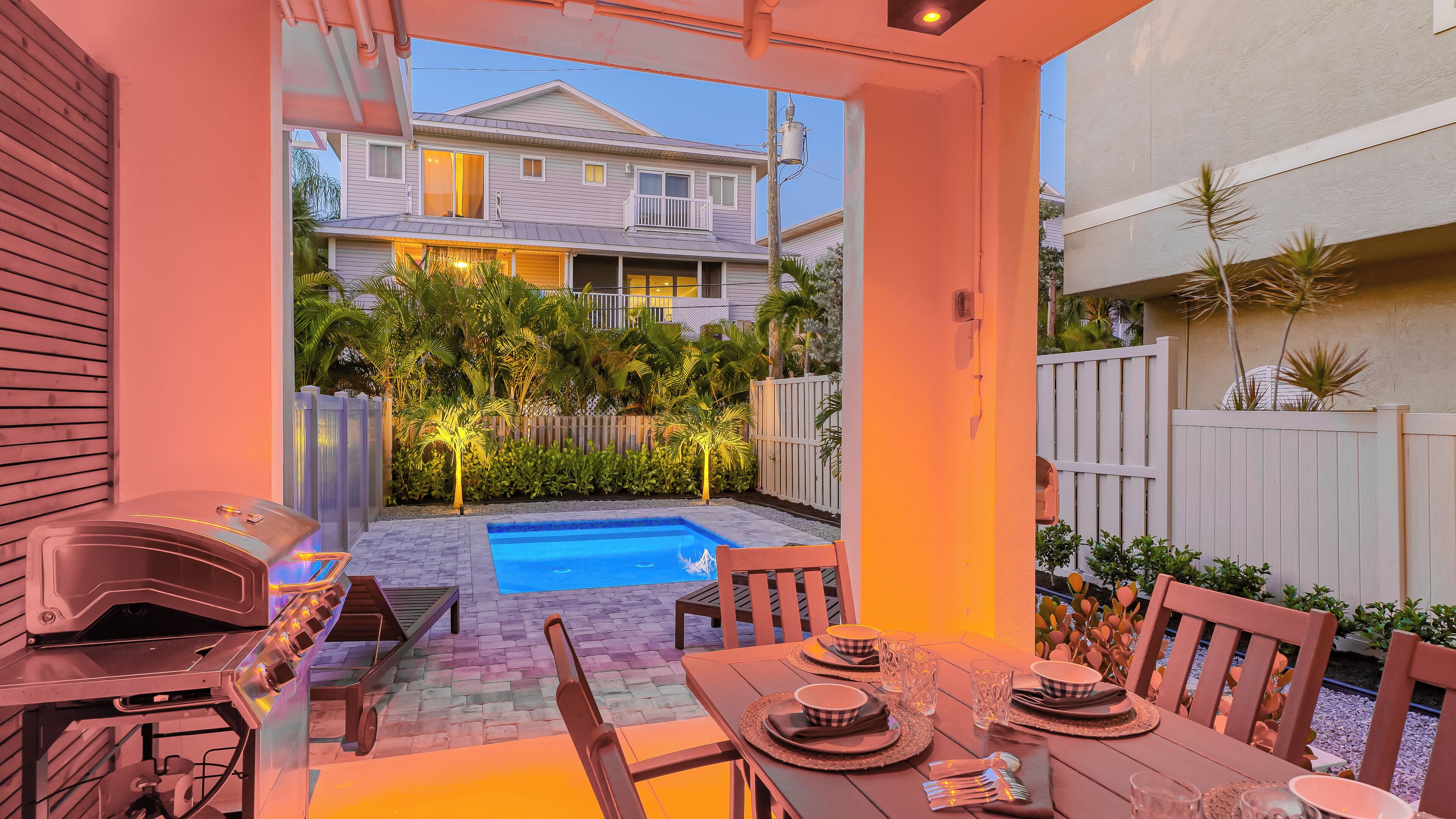 A backyard with a swimming pool, a barbecue grill, and a dining table set for two.