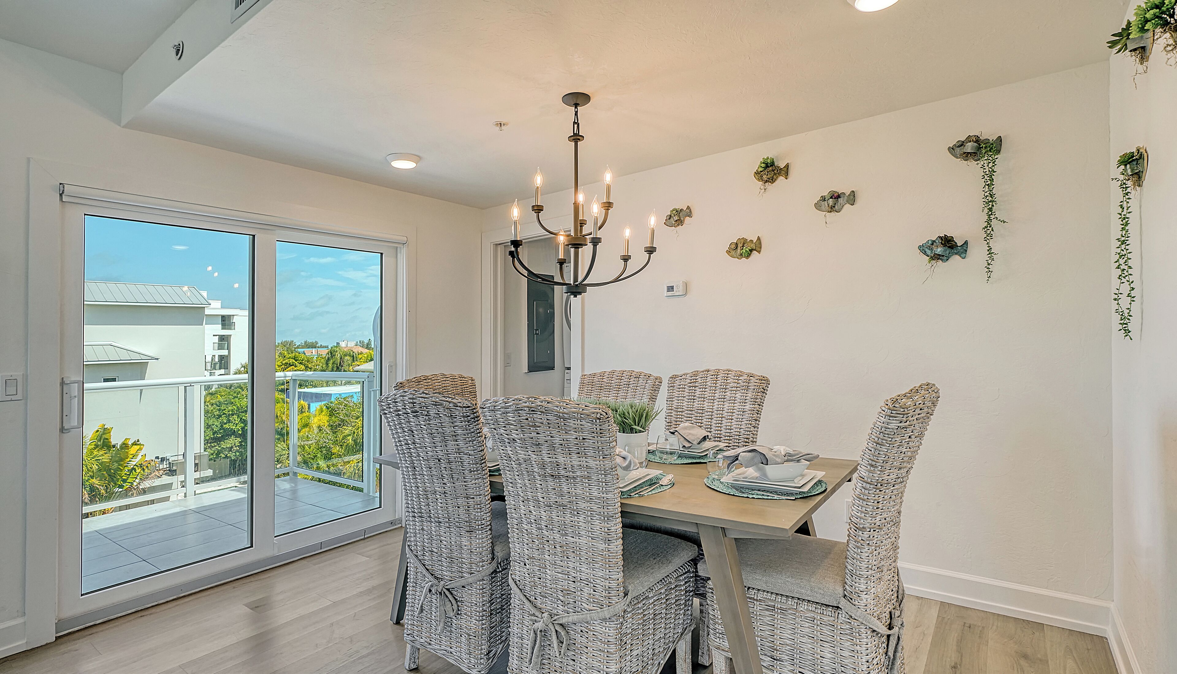 A dining area with wicker chairs, a chandelier, and a view through a sliding glass door.