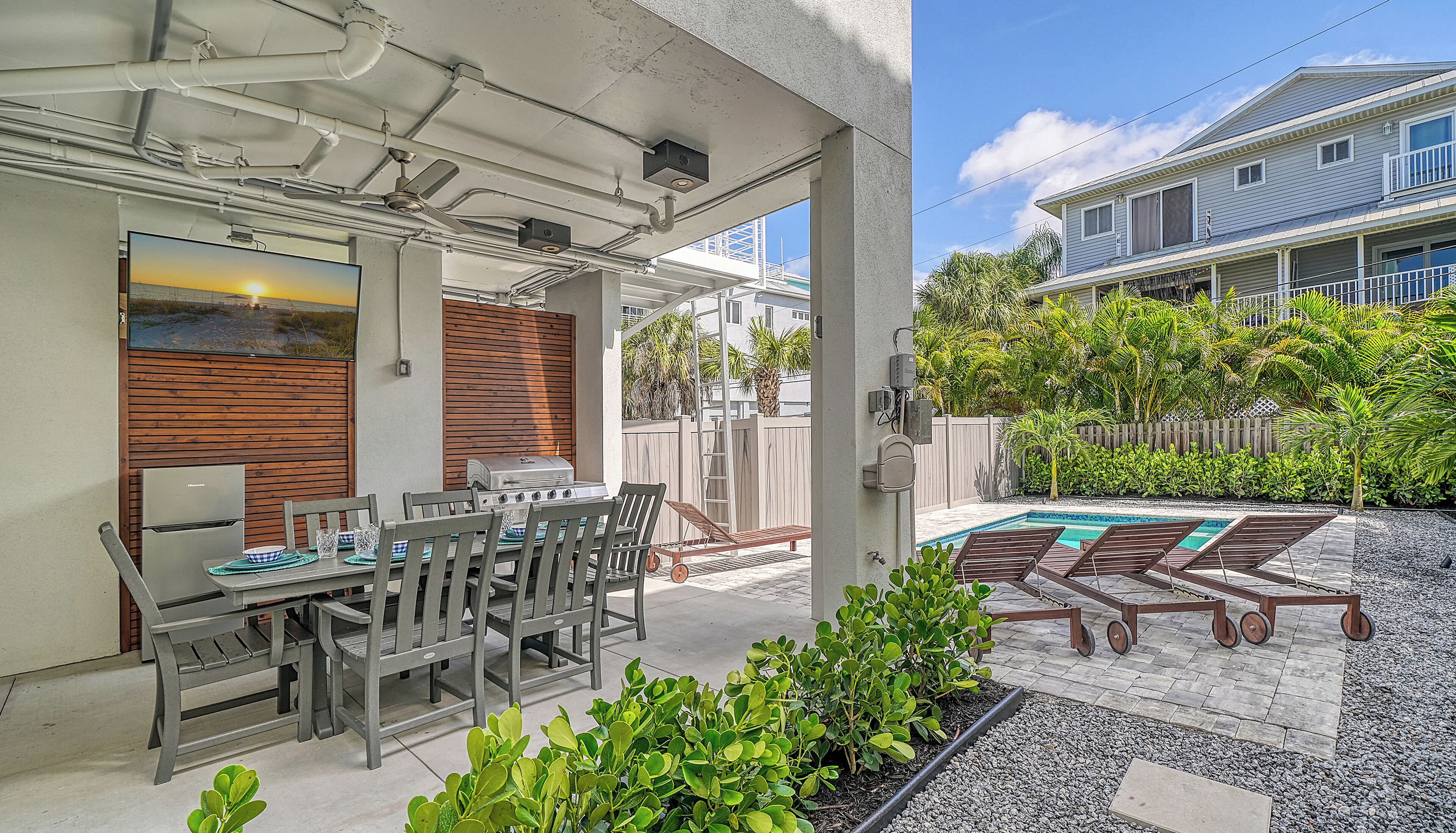 A covered patio with a dining table and chairs, a barbecue grill, and a pool area with lounge chairs.