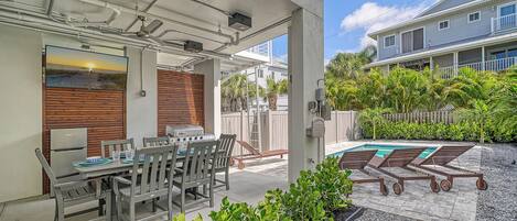 A covered patio with a dining table and chairs, a barbecue grill, and a pool area with lounge chairs.