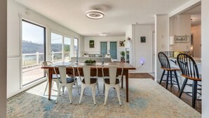 Een eetruimte met een grote tafel, witte stoelen en uitzicht op het buiten.