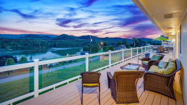Een balkon met rieten meubels en uitzicht op een rivier en bergen.