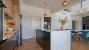 A modern kitchen with a marble island, wooden cabinets, and a dining area with blue chairs. - Cozy home in Grubine with sauna (Grubine)