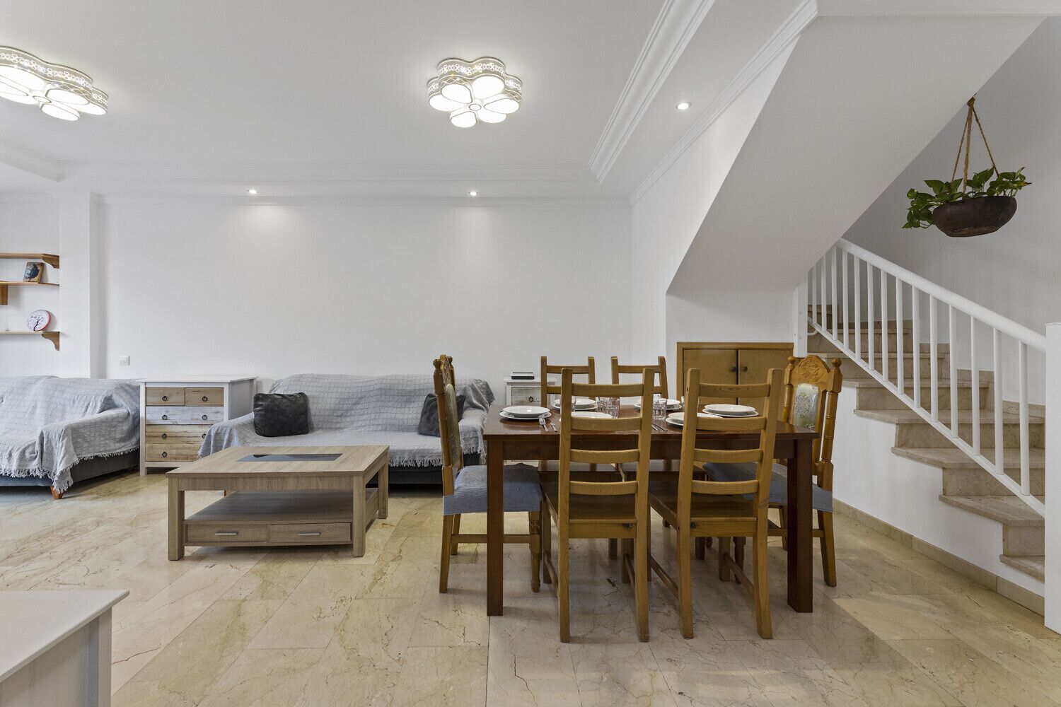 A modern living room with a dining area, a staircase, and a hanging plant.