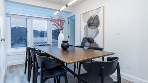A dining area with a wooden table and black chairs, a vase with red flowers, and a large abstract painting on the wall.