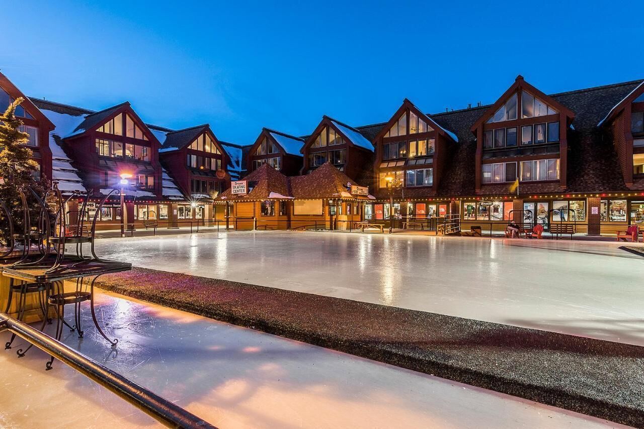 A hotel with multiple chalet-style buildings, a central ice rink, and outdoor seating areas.