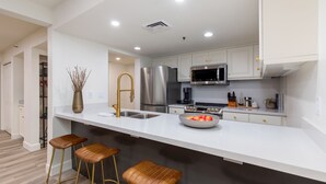 A modern kitchen with white cabinetry, stainless steel appliances, and a central island with stools.
