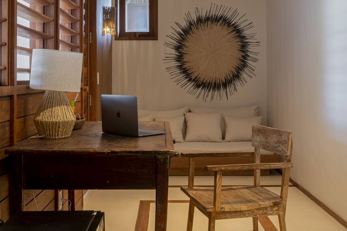 Una habitación con un escritorio de madera, una laptop, una silla, una cama y una obra de arte en la pared.