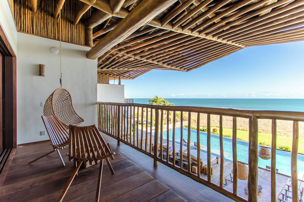 Una terraza de madera con vista al océano, una silla colgante y una zona de piscina.