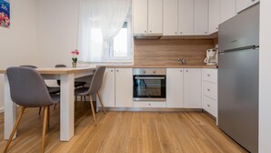 Una cucina compatta con mobili bianchi, un frigorifero in acciaio inossidabile, un forno integrato e una macchina da caffè.