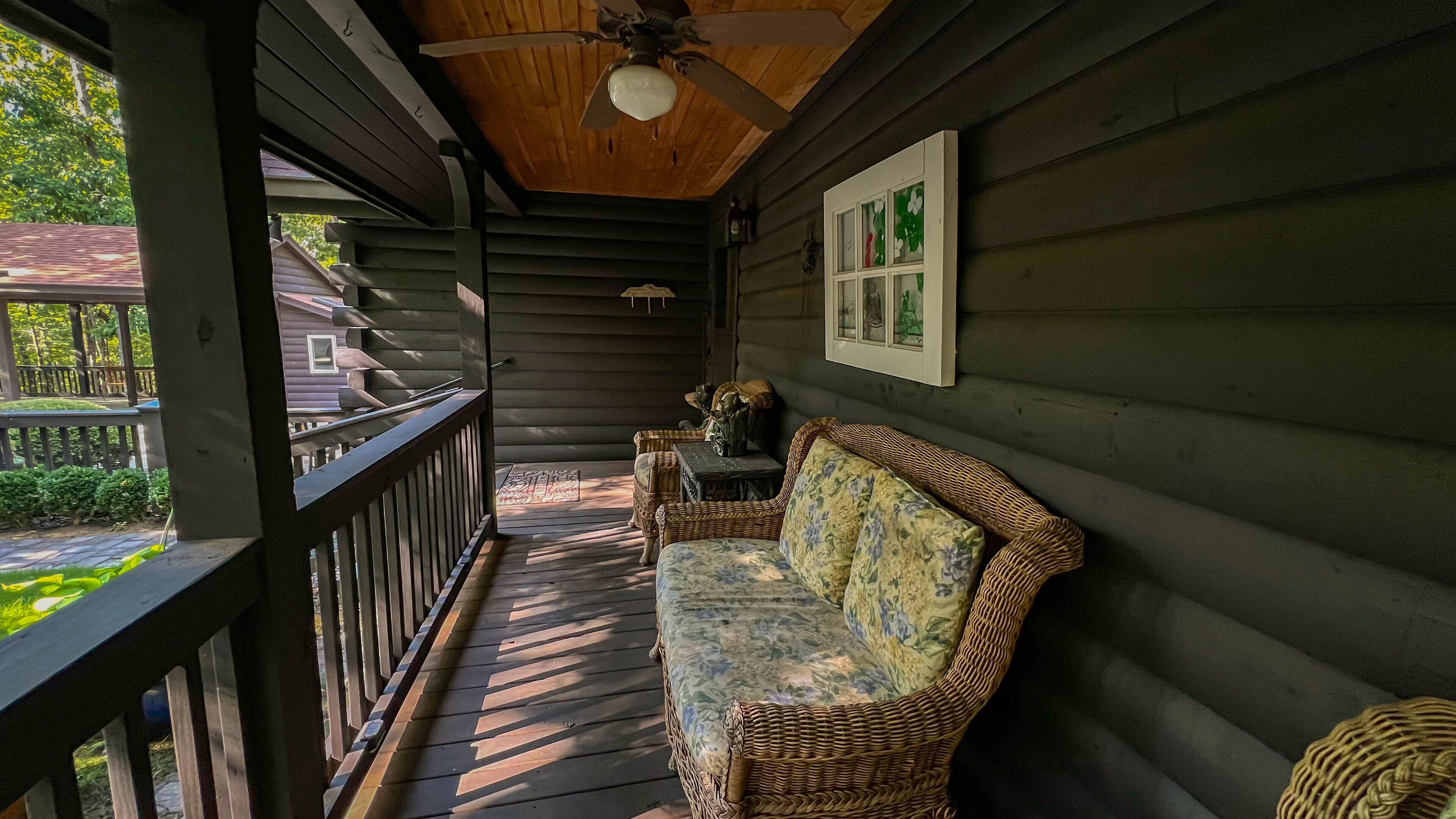 Un porche de madera con ventilador de techo, sofá de mimbre y una mesita.