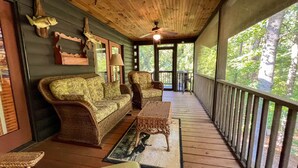 A covered porch with wicker furniture, a ceiling fan, and a view of the surrounding forest.