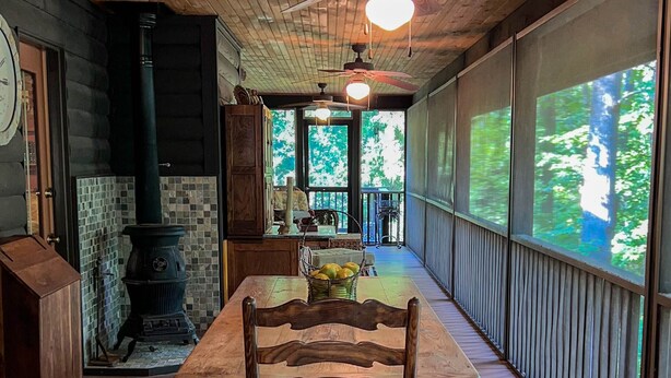 A wooden deck with a table and chairs, a large window, and a fireplace.