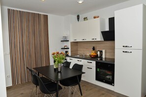 Cozinha moderna com área de jantar, apresentando um painel de ripas de madeira, armários brancos e uma mesa de jantar preta com cadeiras.