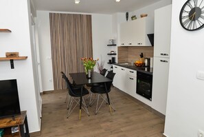Cozinha moderna com armários brancos, uma mesa de jantar preta com duas cadeiras e um relógio na parede.