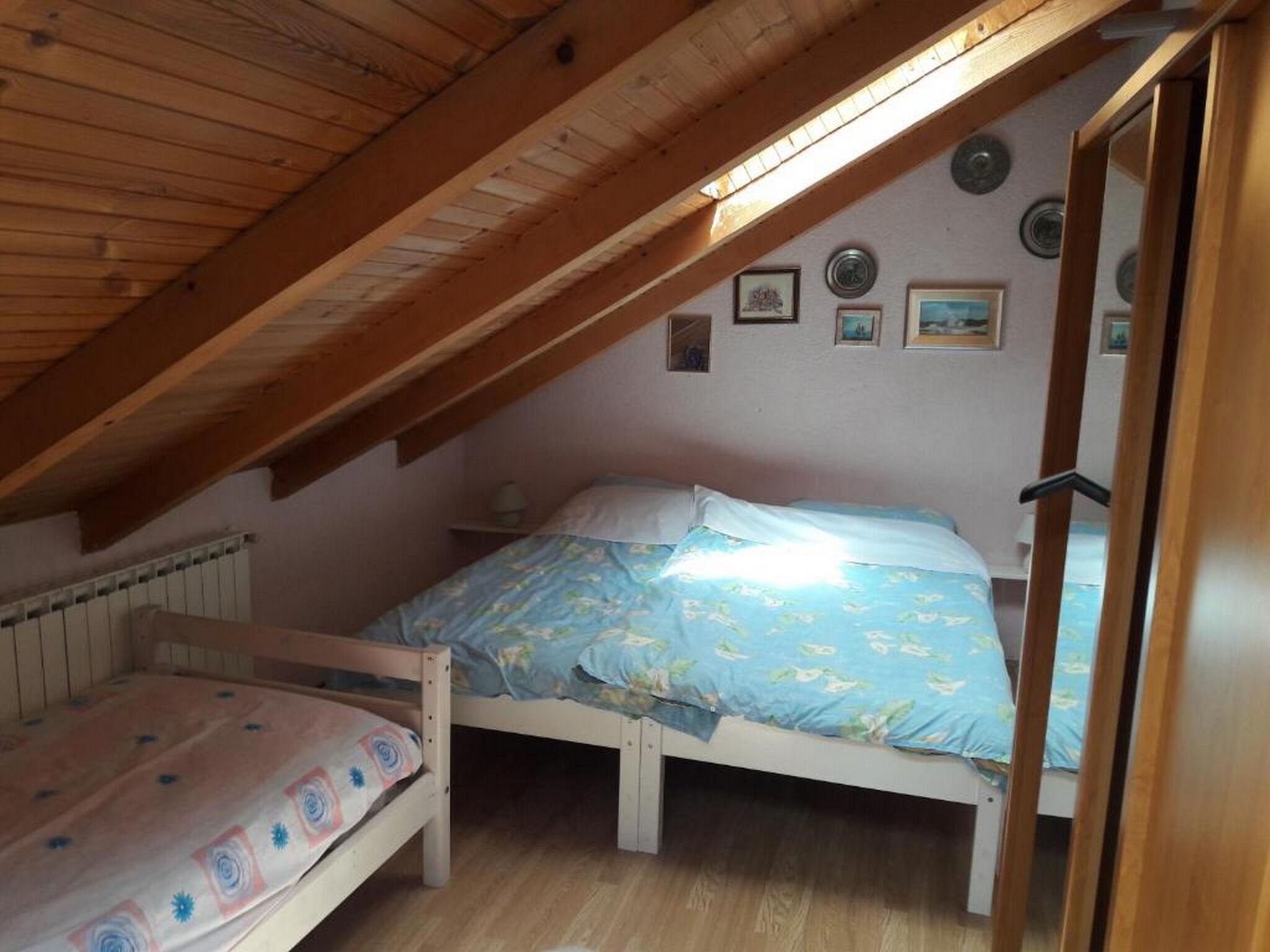 Une petite chambre mansardée avec deux lits, des poutres en bois et un plafond en pente.