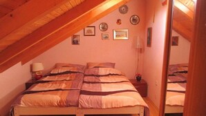A bedroom with a sloped ceiling, a bed with striped bedding, a bedside table with a lamp, and a mirror on the wall.