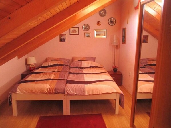 A bedroom with a sloped ceiling, a bed with striped bedding, a bedside table with a lamp, and a mirror on the wall.