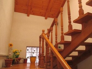 A wooden staircase with a handrail, leading to an upper floor. There are potted plants on the landing.