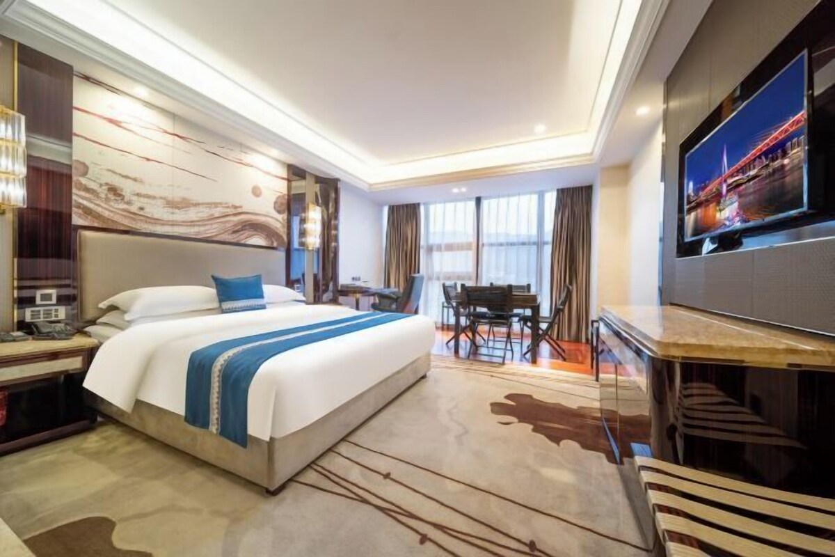 A hotel room with a bed, a desk, a chair, a TV, and a large window.