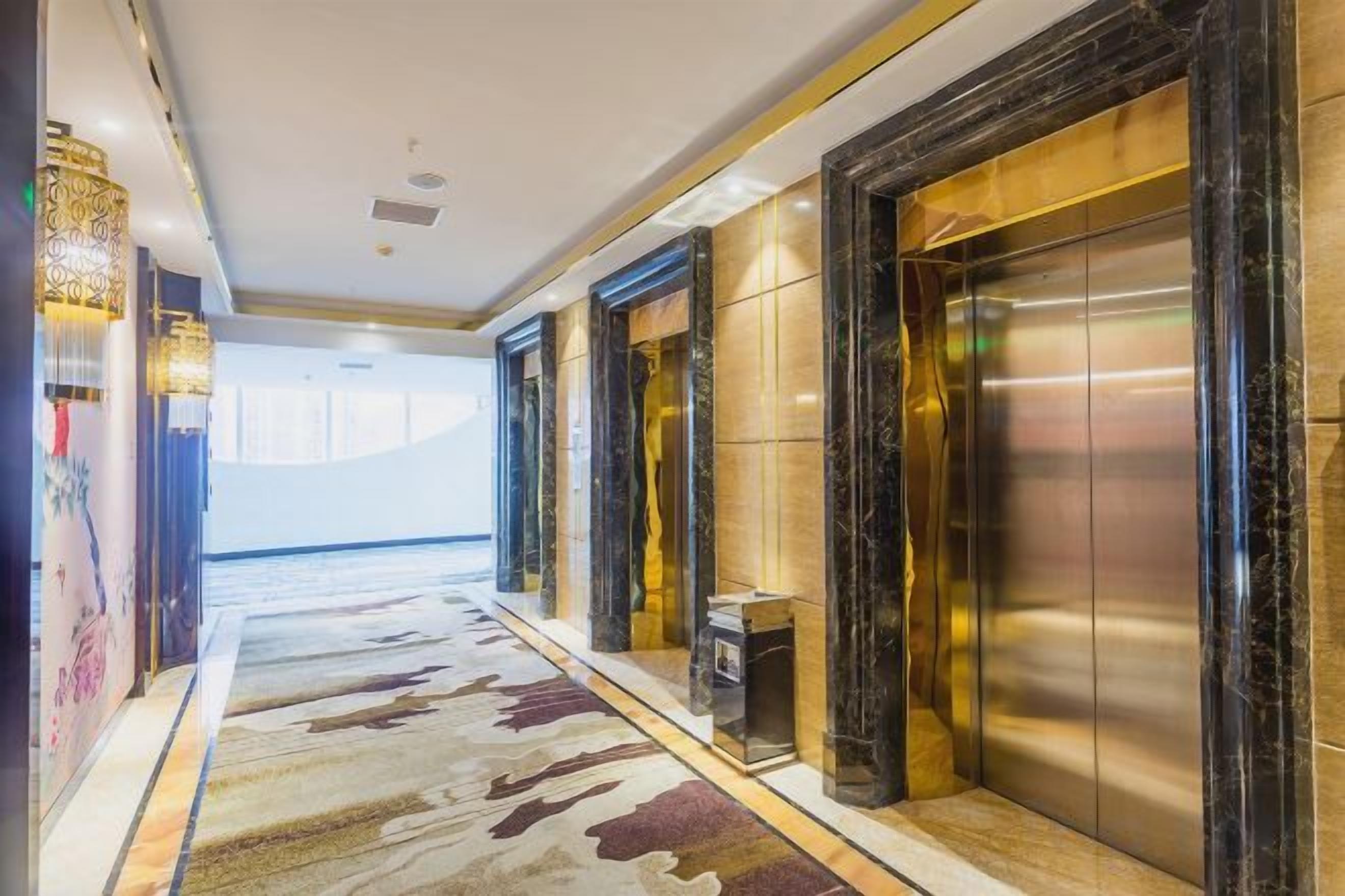 A hotel lobby with a marble floor, elevators, and a reception desk.