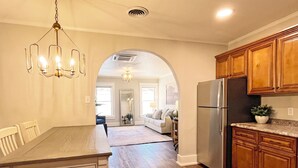 A modern kitchen with wooden cabinets, a stainless steel refrigerator, and a dining area with a table and chairs. - Full Kitchen // Spacious Living Room // Walk to Mineral Springs and Restaurants (Hot Springs)