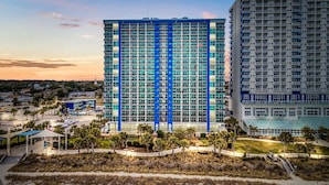 A high-rise hotel with multiple floors, a parking area, and a beach in the foreground. - Guest Favorite ~ Newly Renovated ~ 18th Floor Direct Ocean + SkyWheel Views (Myrtle Beach)