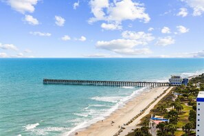 A beach with a pier extending into the ocean, a building with a blue roof, and a clear sky.